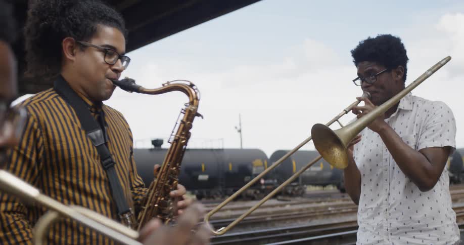 Three young men play instruments near a train