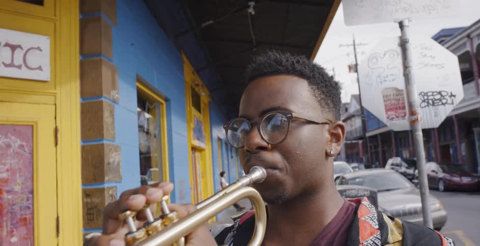 Black boy who wears glasses plays saxophone in the street on a cloudy day