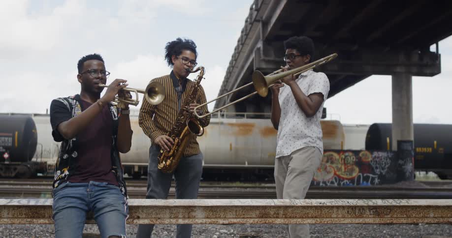 Three young men playing instruments near a train