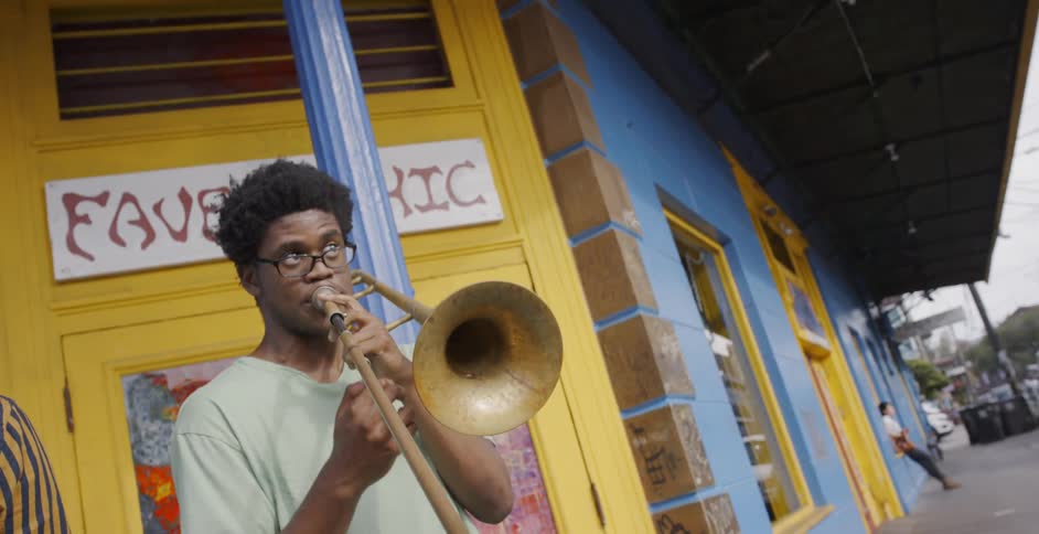 Young black man plays trombone on street corner in front of colorful building
