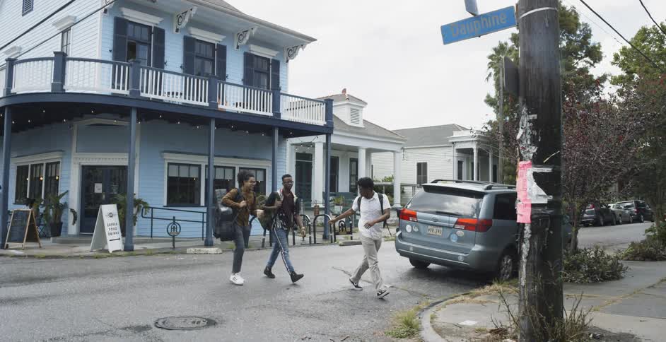 Three young black men walk across a neighborhood street while bantering with one another