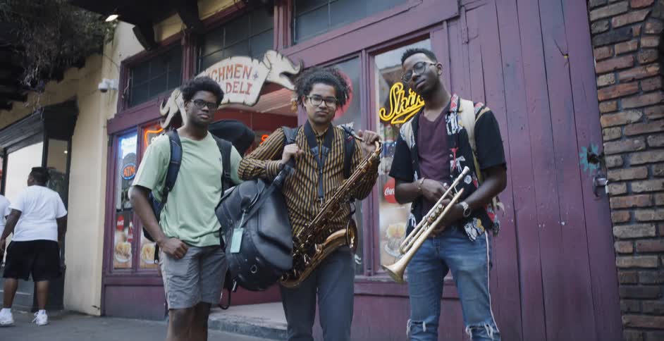 Teenagers posing in front of a store with two of them holding an instrument