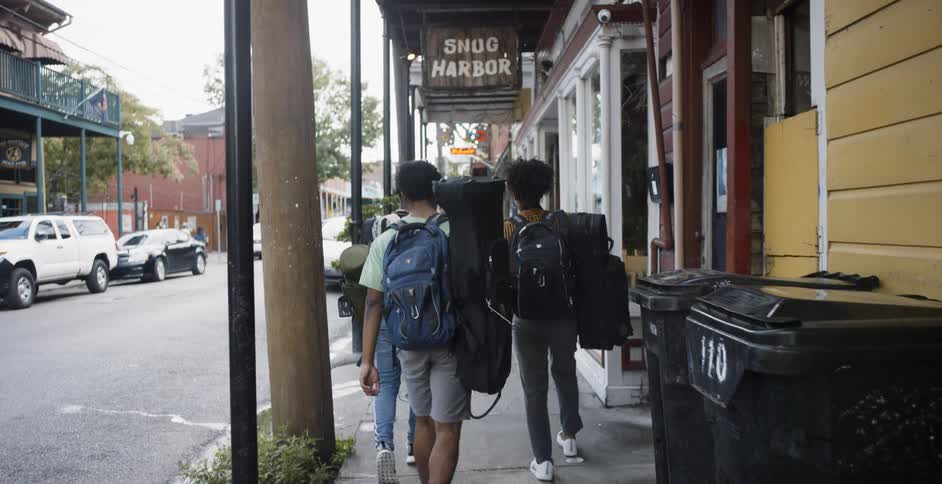 Teenagers walking down a street holding instruments