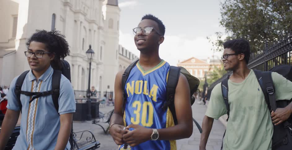 Group of black friends having fun and walking down a sidewalk while carrying their musical instruments on backpacks
