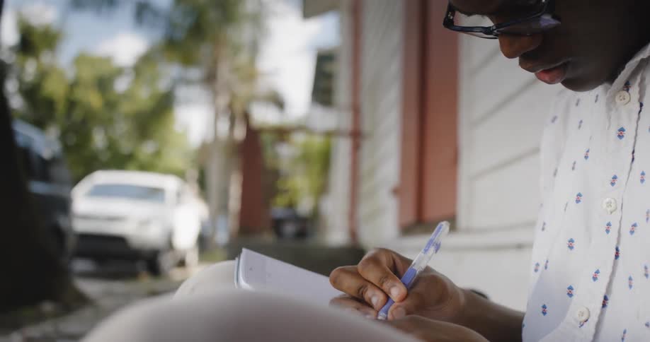 A black man sitting outside writes in a notebook