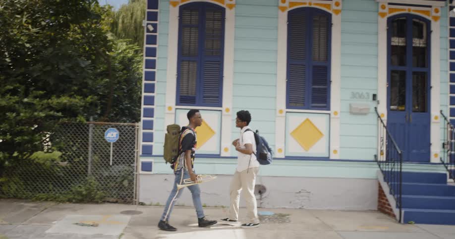 Two young black men walk down a sidewalk while conversing