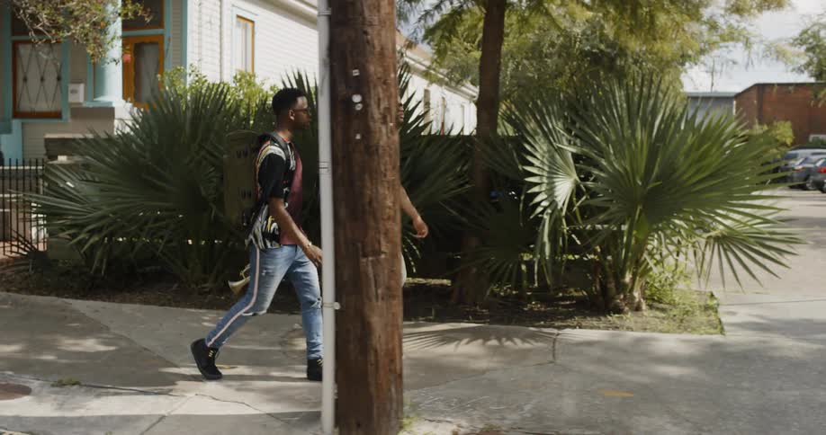 Two young black men with backpacks walk and talk on neighborhood sidewalk