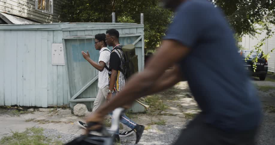 Two males walking passed a wooden fence with many cars parked inside