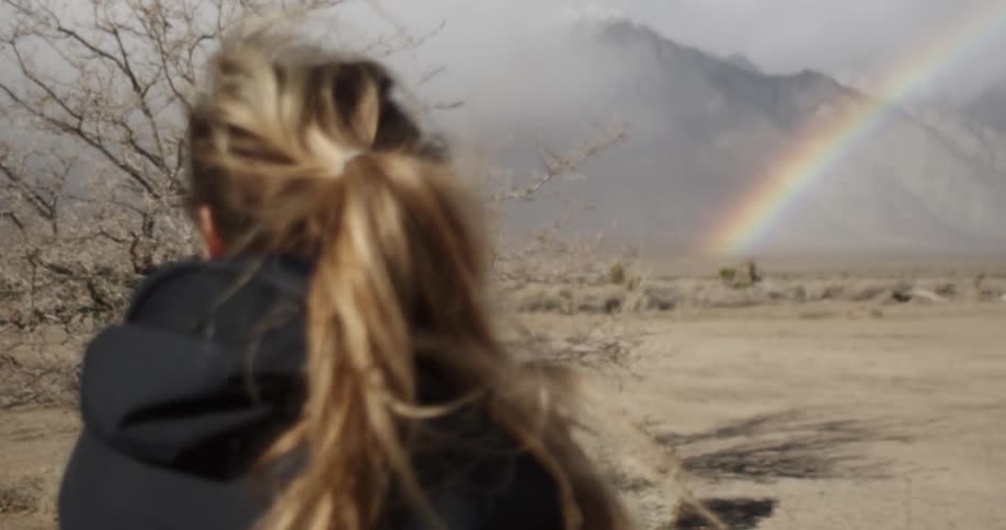 Woman looking at a rainbow in the distance on a deserted plain