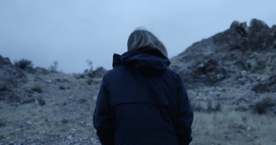 Woman wearing jacket hikes up rocky barren mountain