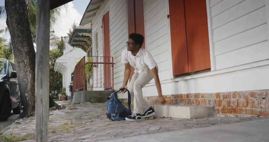 A man outside getting up and putting on a backpack