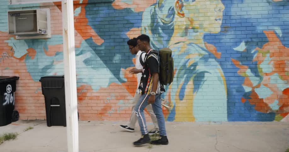 Two men walk next to a wall mural