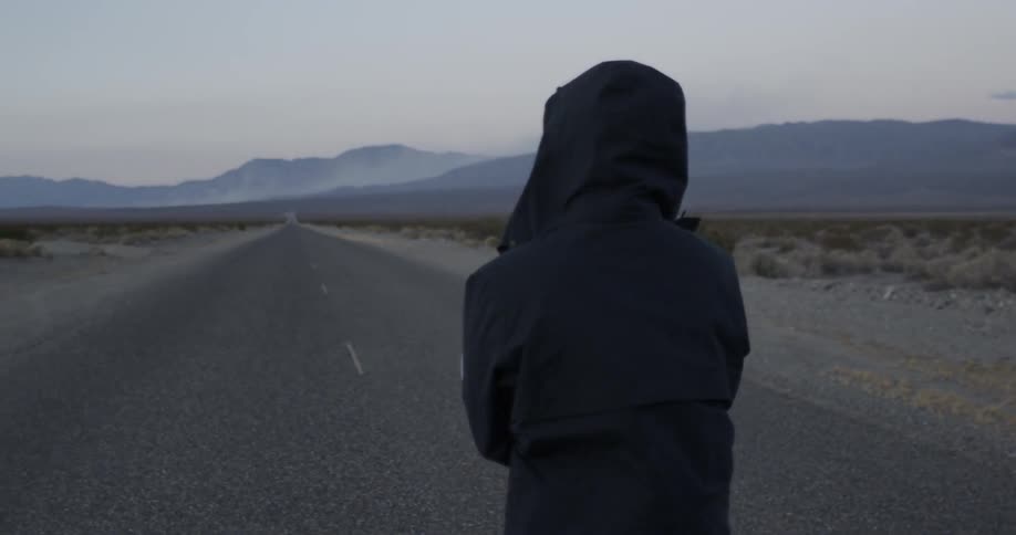 Person stands on a desolate road looking down it