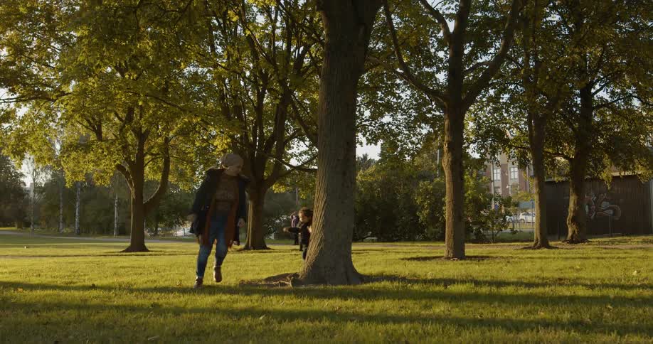 Mother and daughter run around tree in park in afternoon sunlight