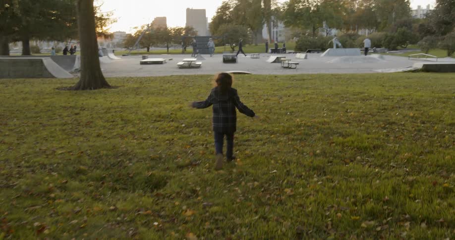 Toddler runs through a field of grass with autumn leaves at sunset