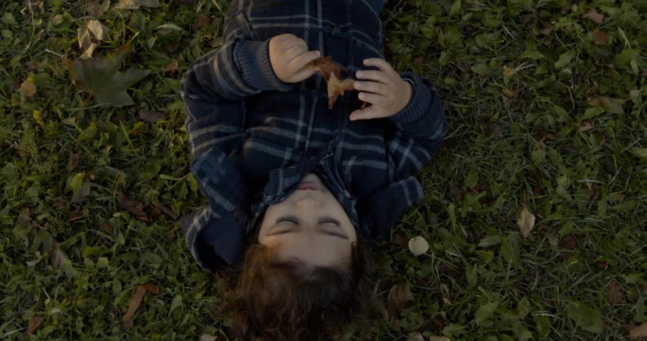 A child laying on grass holding a leaf