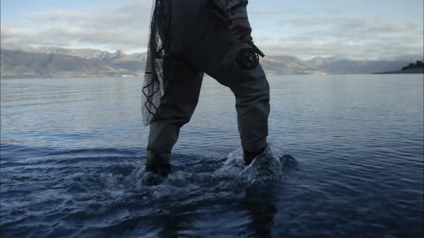 A fisherman wades through shallow water carrying his fishing pole and a net