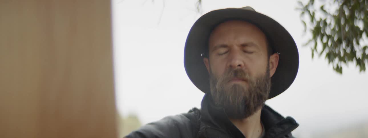 A bearded man paints a landscape while outdoors
