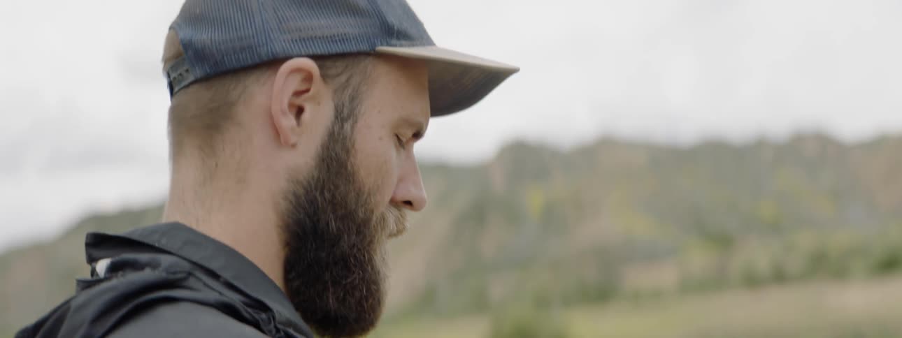 A man with a beard and wearing a hat looks up at something in the sky