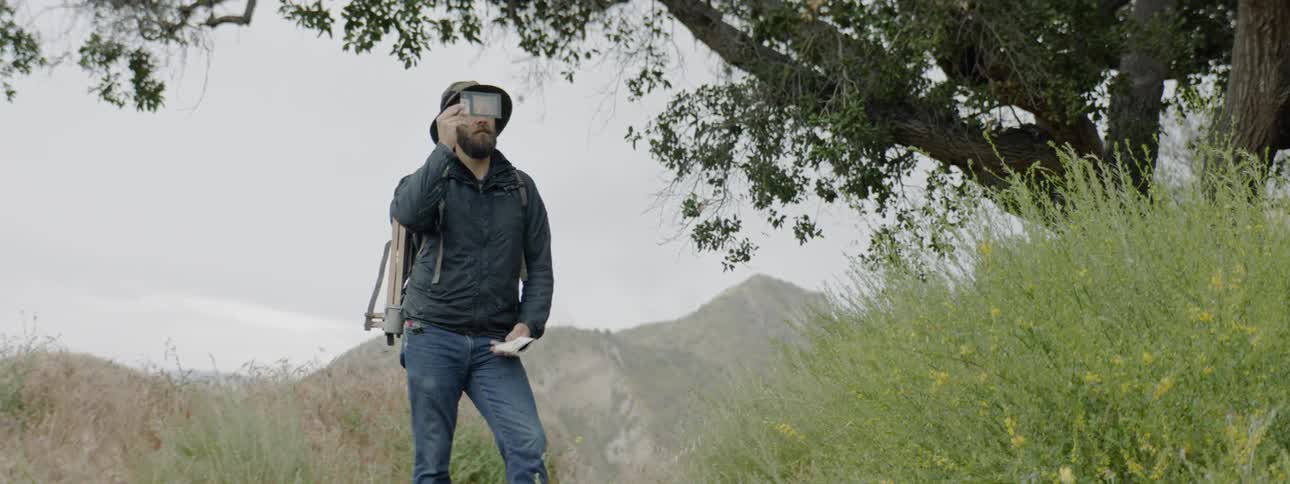 A man takes notes in a notebook while standing in a field