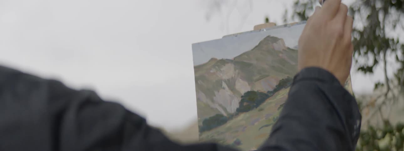 Man works on landscape painting on canvas outdoors