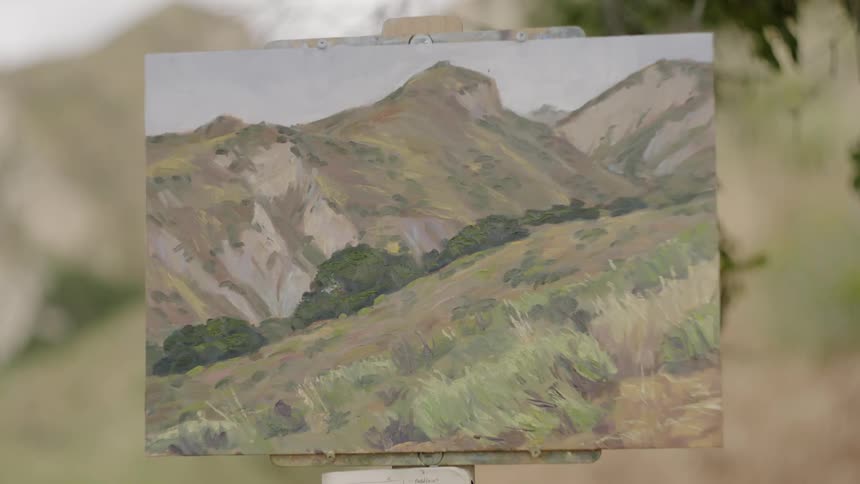 A canvas with a painting of a meadow and mountains