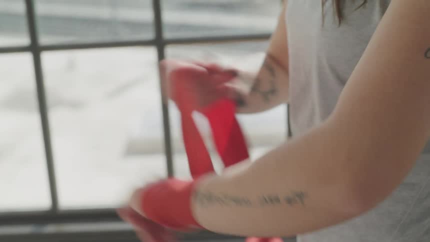 A woman wraps her hand and wrist with red athletic tape