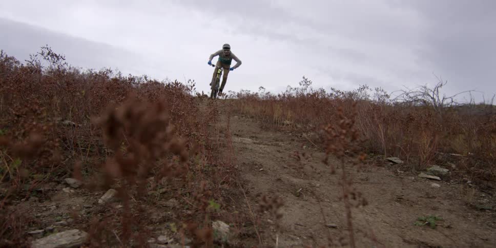 Man riding a bicycle down a weed-covered hill