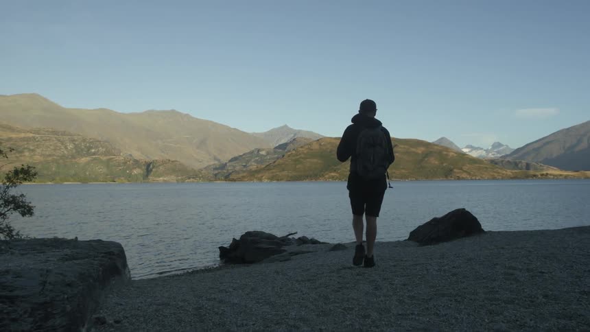 A man walks along the shoreline surrounded by mountains