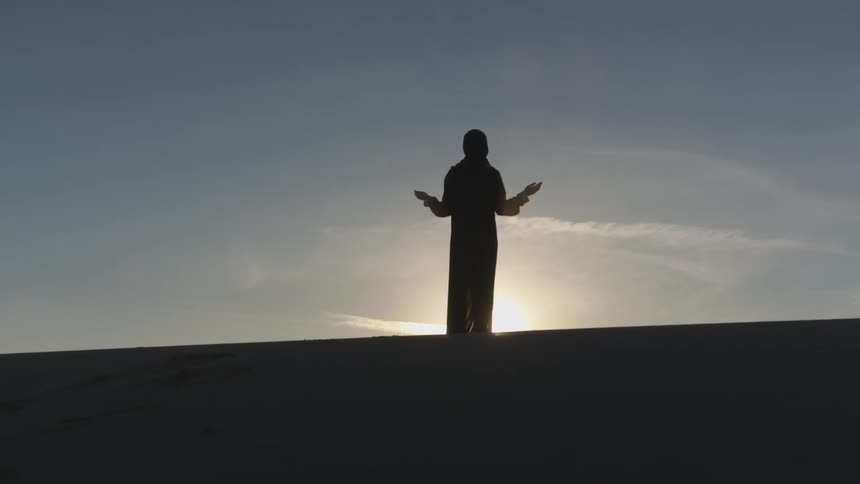 A person praying or meditating on a hilltop during sunrise