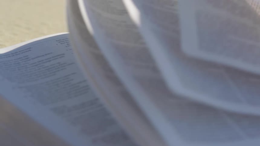 The pages of a bible flip in the wind on a sunny day