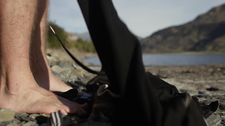 A man stands along a rocky shoreline dropping his wet suit