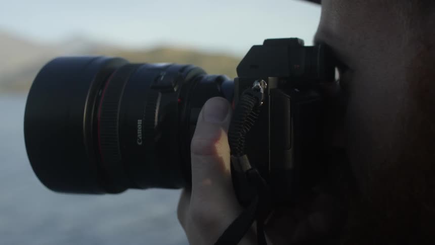 A bearded man photographs a mountain lined lake