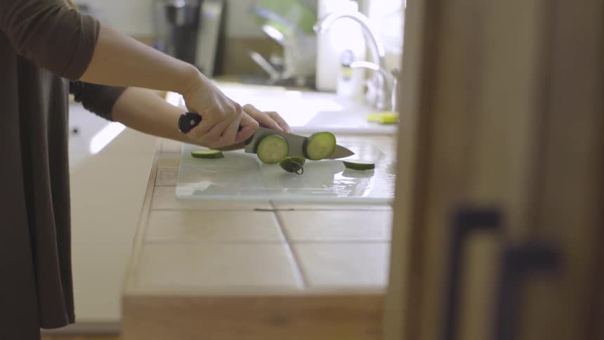 A woman cutting cucumbers in a kitchen