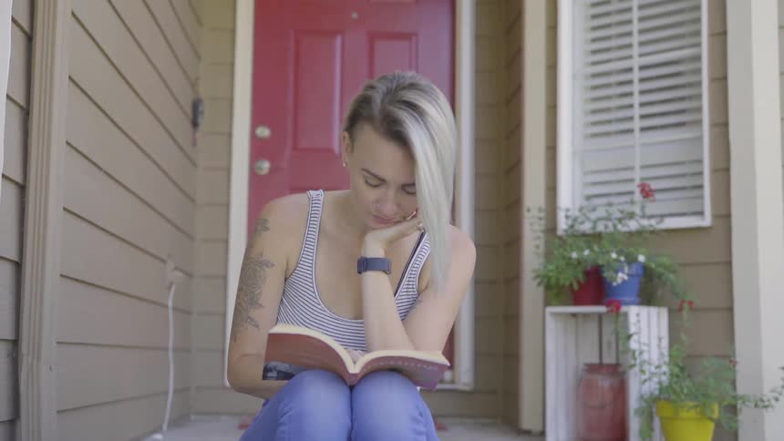 Blonde hair woman sits on stairs in front of a red door