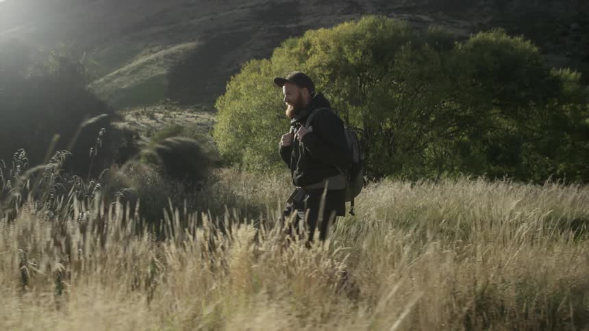 Man carries backpack while hiking through tall grass