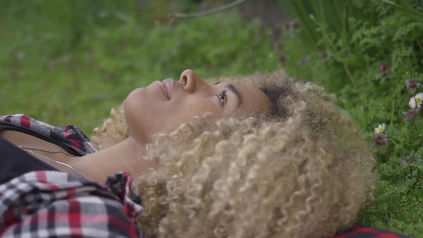 A young black woman lies on the grass looking up