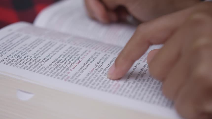 Person puts finger on page of the book and reads indoors by day