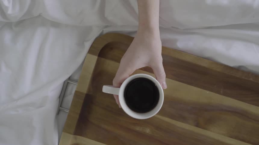 A white hand reaches out and grabs a cup of coffee