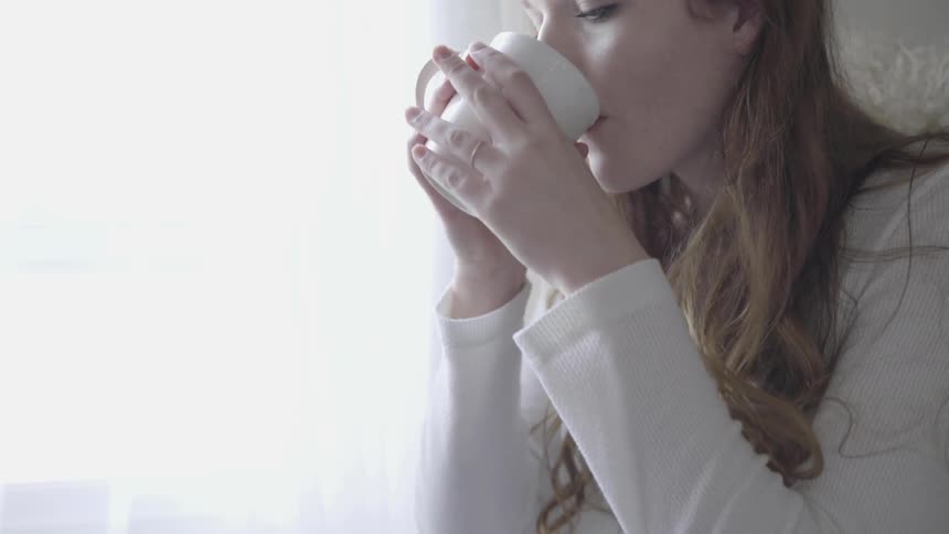 Woman sips from mug near window