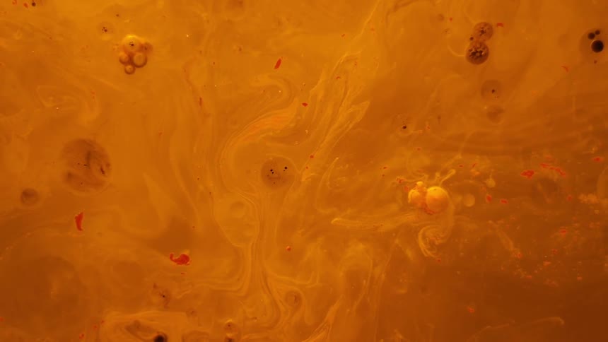 Bubbles burst and form in orange liquid
