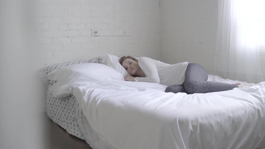 A woman lies awake in bed in a white room