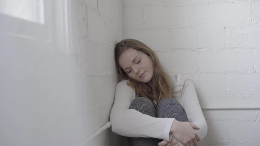 A woman sits sadly in the corner