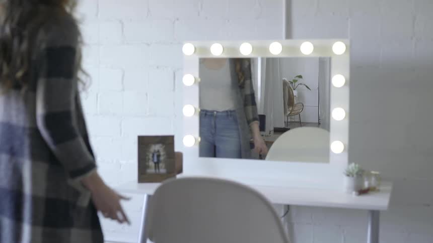 A female sitting down at a lighted mirror and table