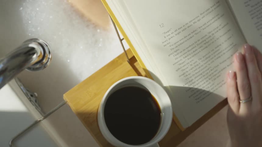 A woman drinks coffee and reads while taking a bubble bath