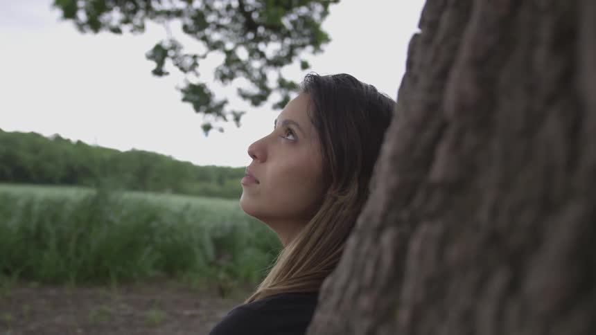 Blonde female looking up the sky while sitting and leaning on a tree
