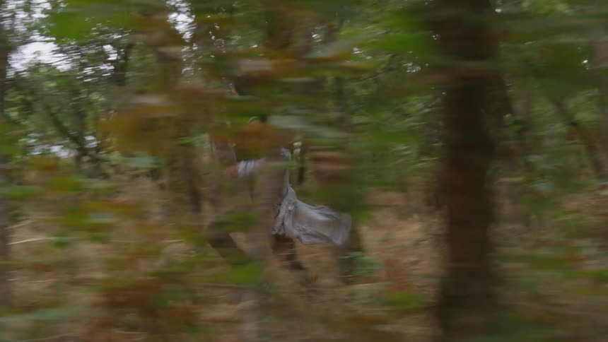 A scared woman sprints through a forest