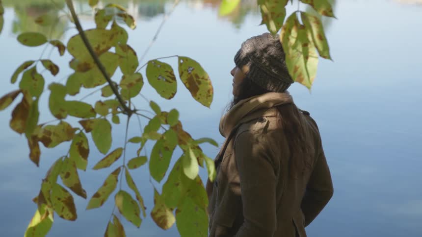 A woman behind a branch is standing and staring out onto a lake