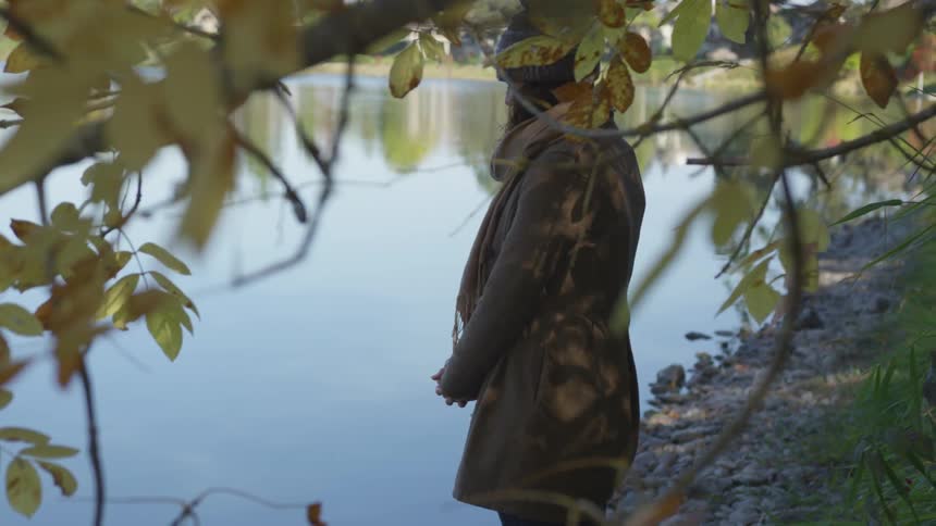 Woman quietly standing next to a lake looking down