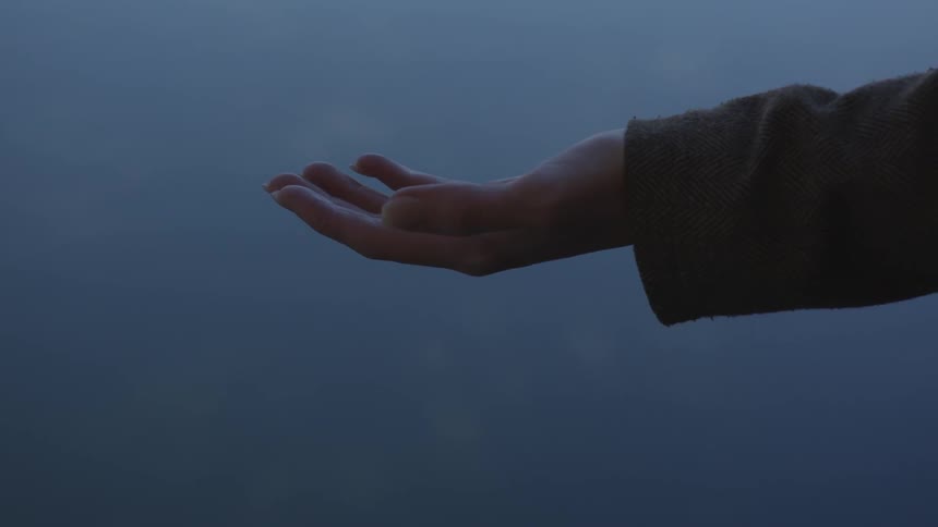 A woman wearing long sleeves holds her hand out palm up on a foggy gray day